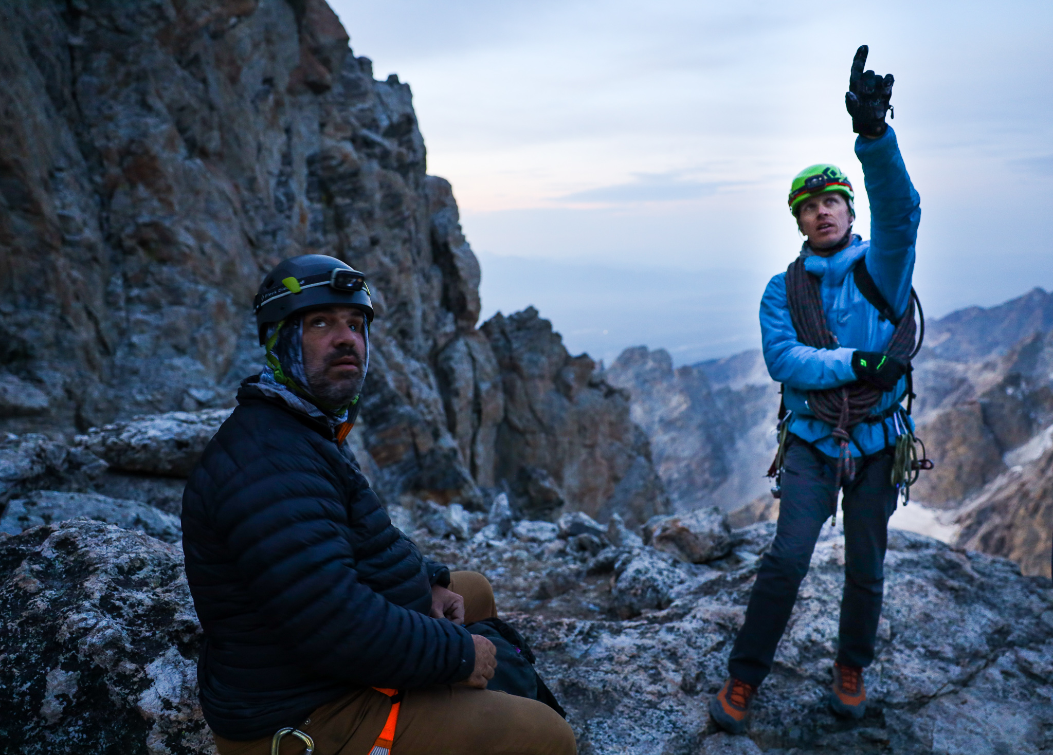 Co-founder DJ, sitting and looking towards the camera with a guide pointing up towards the route in Grand Teton NP