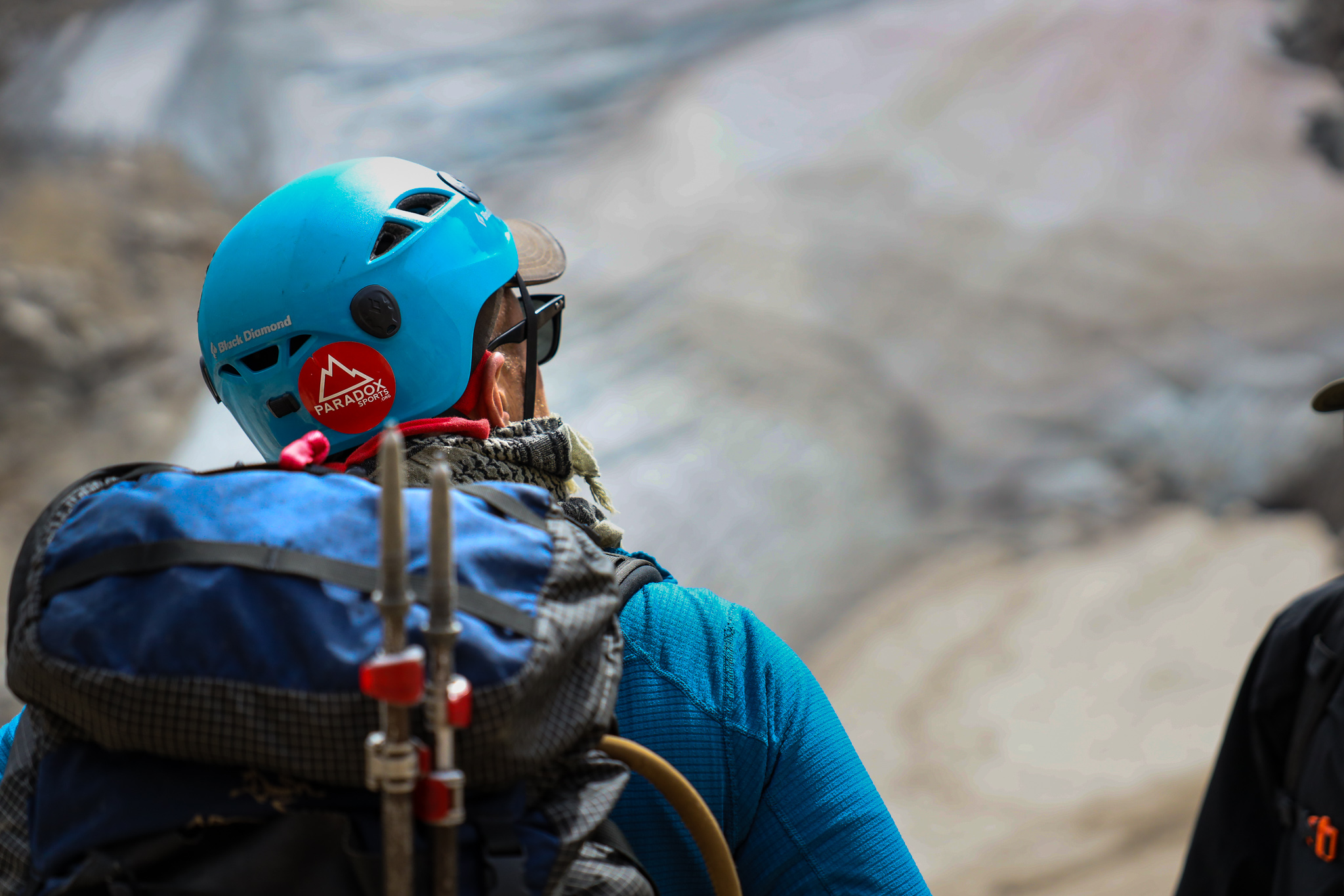 A participant, stands, facing a rock wall weaing a blue helmet with a Paradox Sports sticker on the back