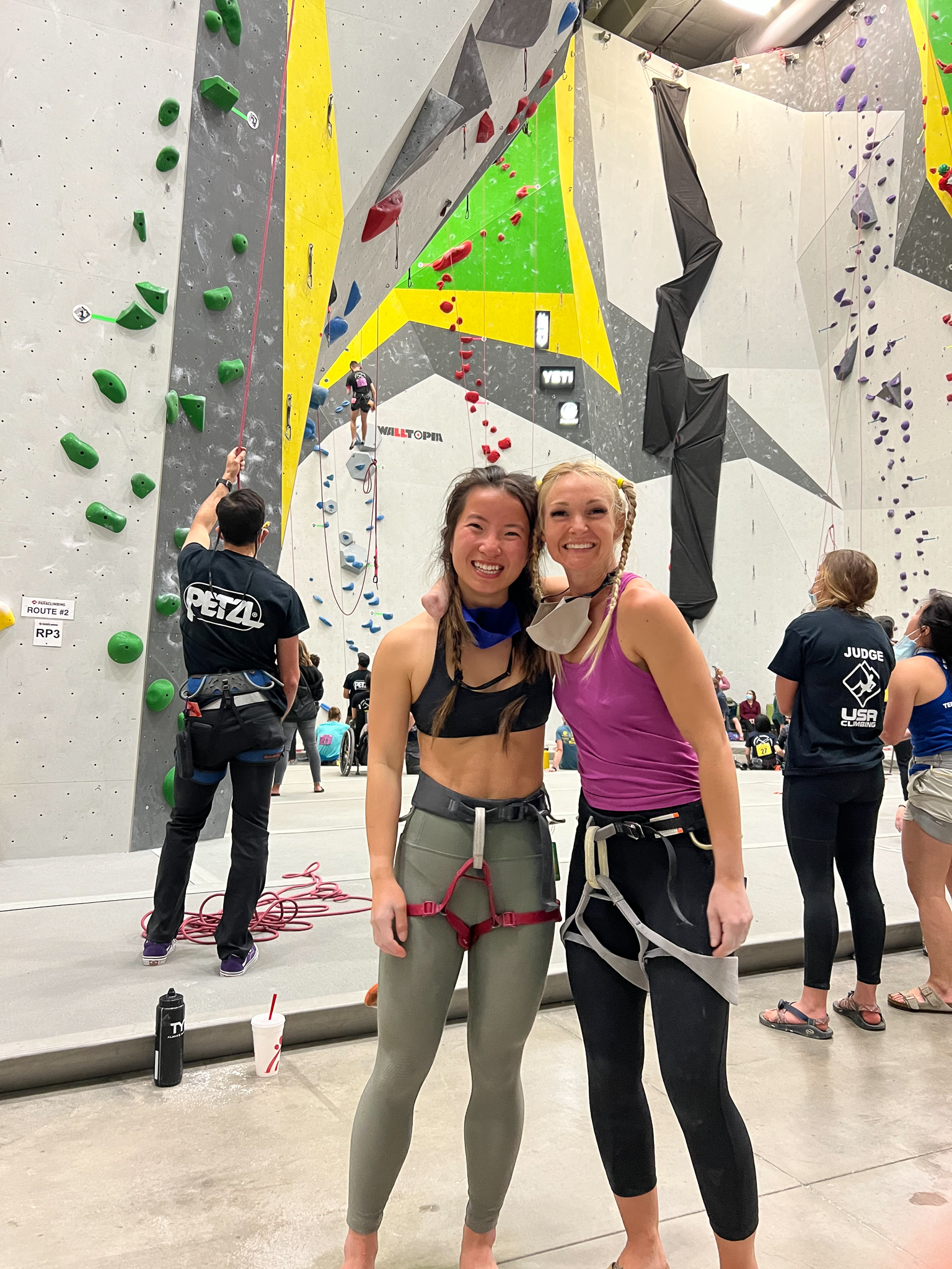 Paradox AAF recipient, Grace, at paraclimbing Nationals, standing in front of a gym wall with a friend