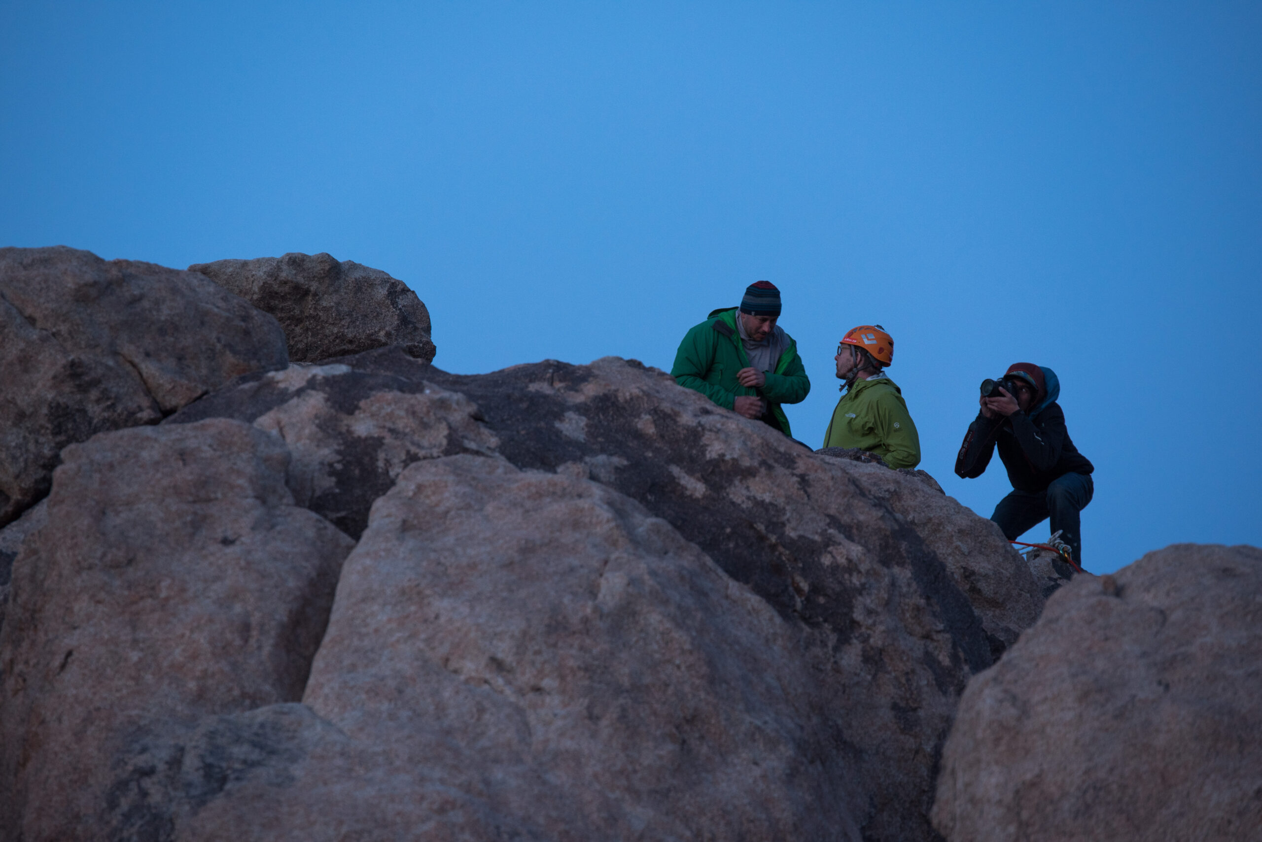 Redish colored rocks in the foreground and 3 people are on top of a route. One is taking a photo of the others.