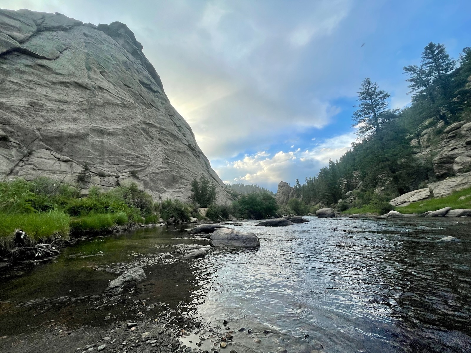 Image of Elevenmile. A rock wall is on the left and a river is to the front and right, lined with boulders and trees on the far right.